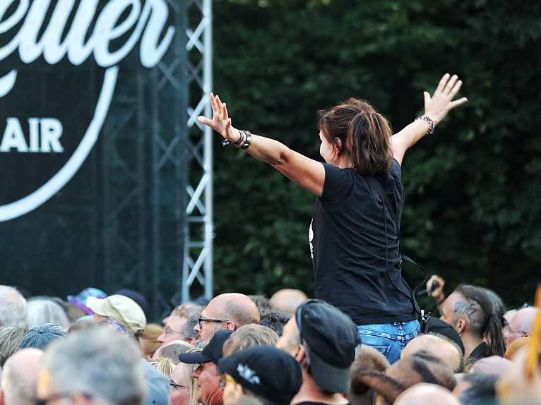 Eine Frau auf den Schultern anderer Menschen im Publikum vor einer Bühne.